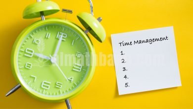 Jam alarm berwarna hijau dengan kertas catatan kecil bertuliskan "management", ilustrasi pengingat manajemen waktu.